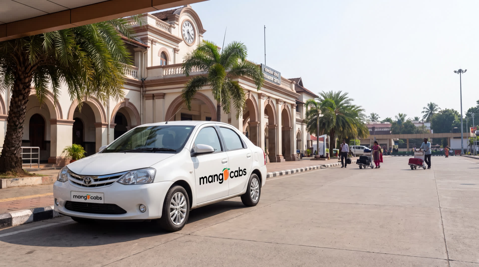 A white Mango Cabs Toyota Etios waiting under the portico at Trivandrum Central railway station, the clock tower and arched heritage frontage behind it